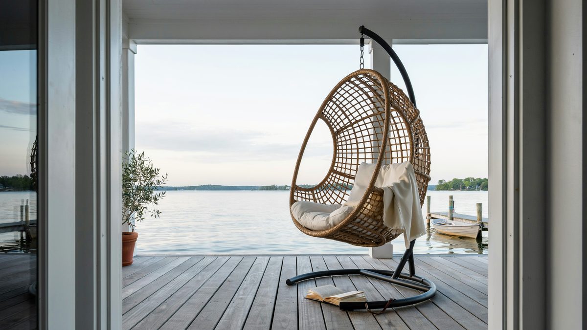 Stand mounted rattan egg chair on a lakeside deck facing open water