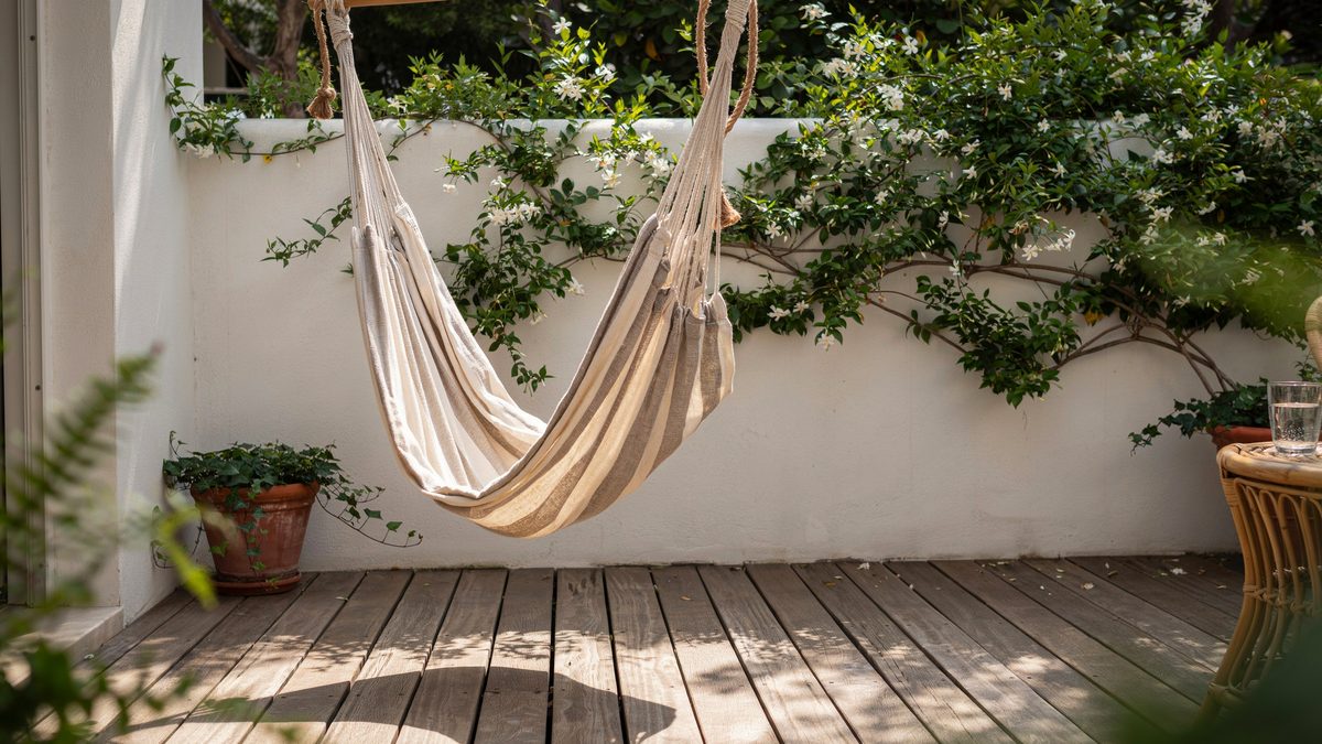 Striped fabric sling hammock chair on a shaded deck beside flowering jasmine