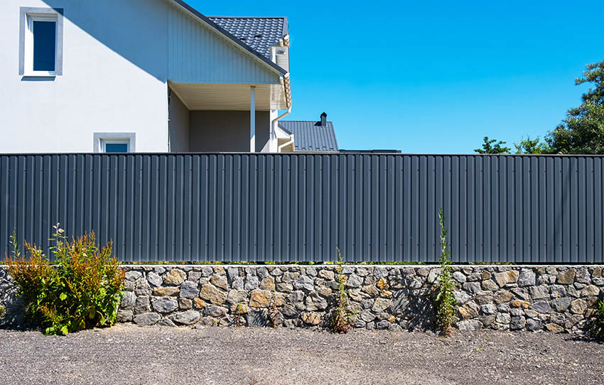 Corrugated metal fence above rock wall around house