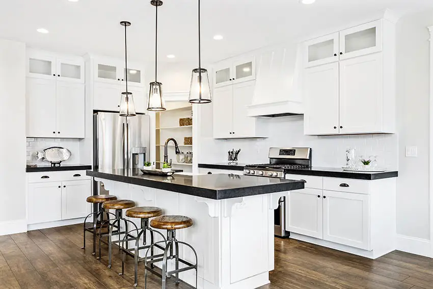 Kitchen with black laminate countertops white shaker cabinets wood plank flooring pendant lights