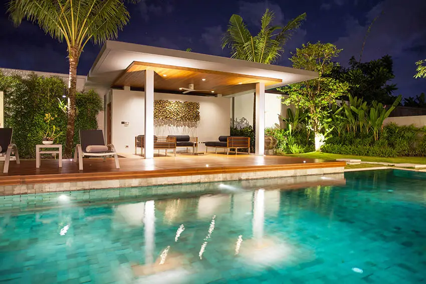 Luxury tile swimming pool with pavilion, wood deck, sofa lounge chairs, and palm trees