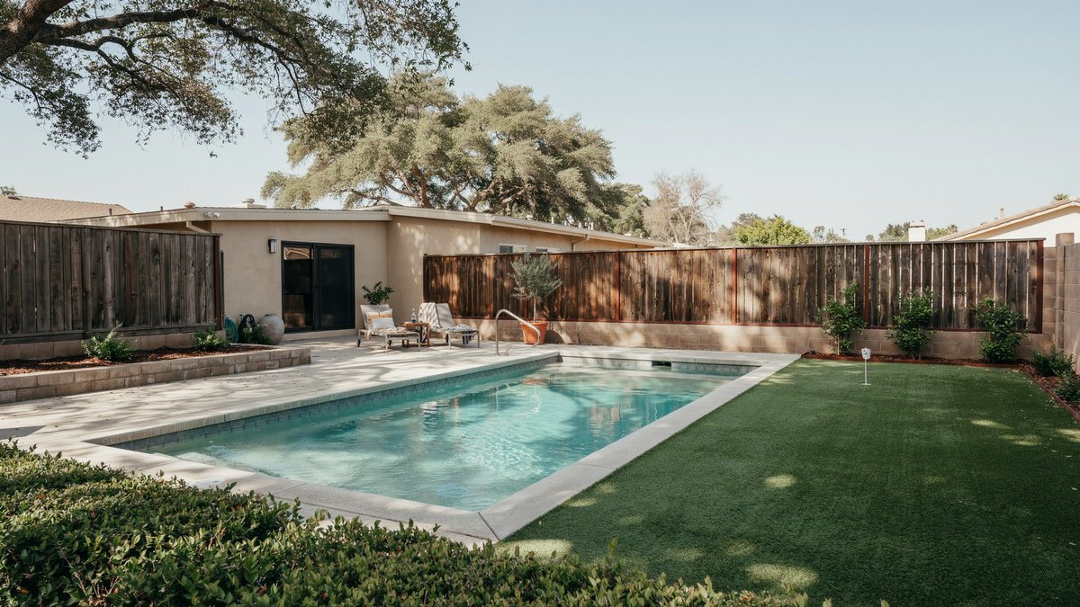 Ranch house pool with turf green and single flagstick along wood fence