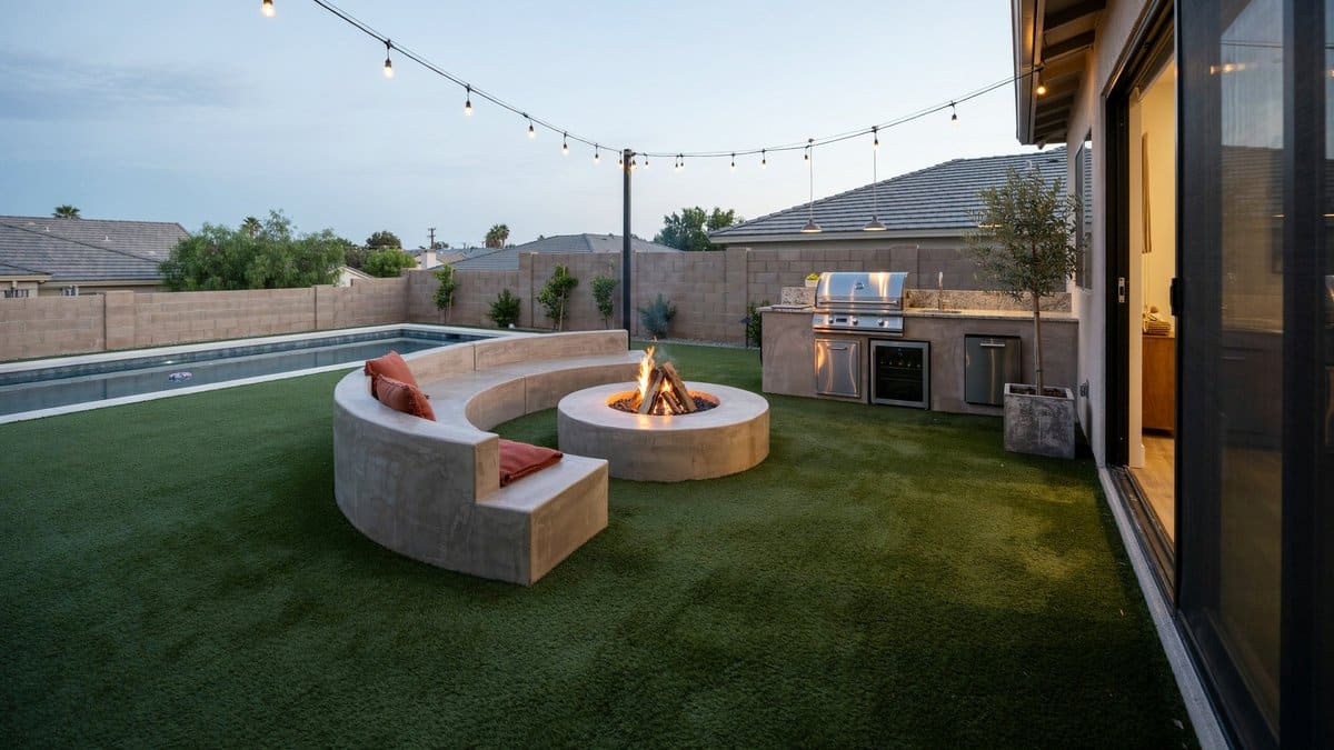 Curved concrete bench circling a fire bowl on turf near outdoor kitchen