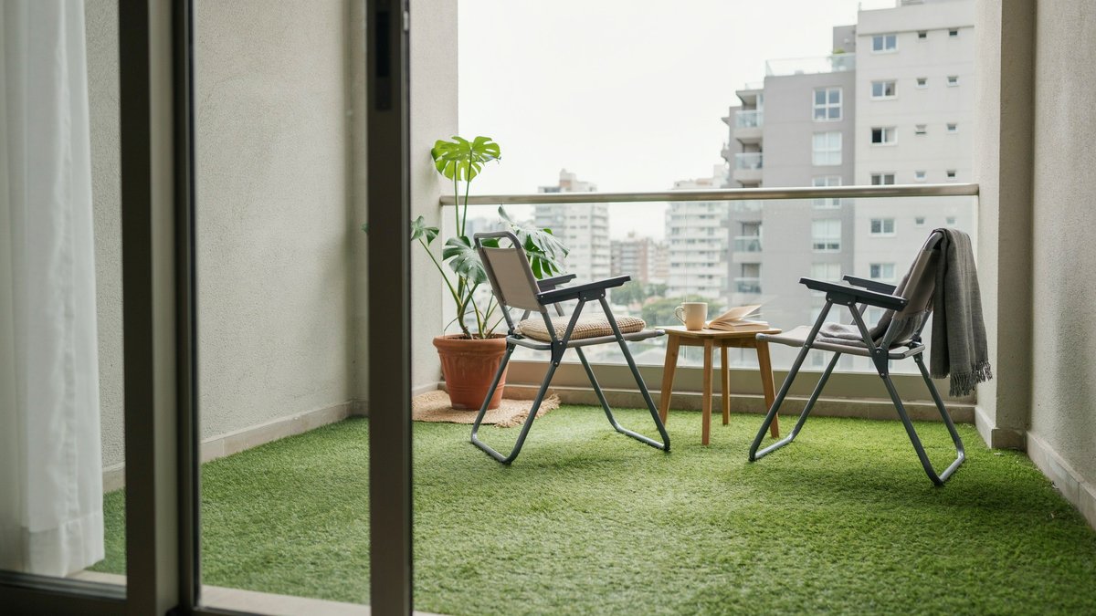 High rise balcony floored in turf with folding chairs and potted greenery
