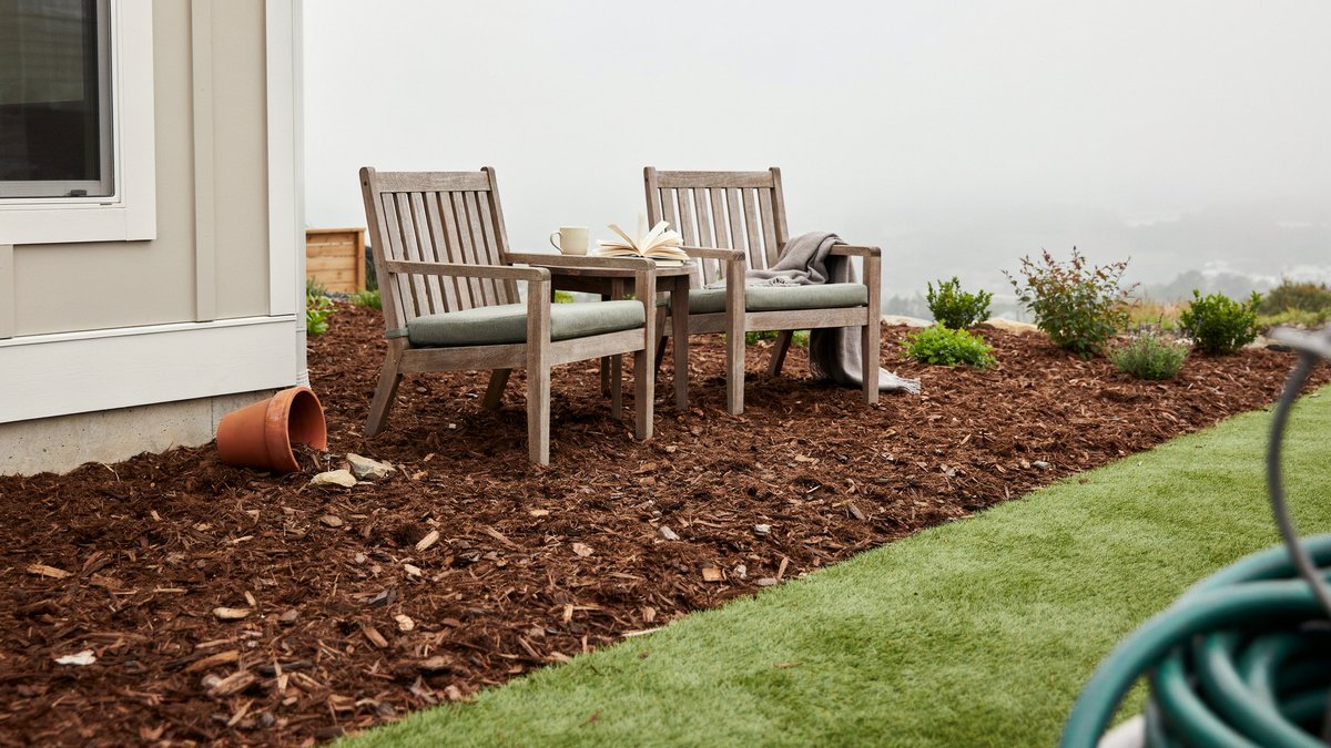 Teak chairs on red bark mulch meeting a strip of green turf
