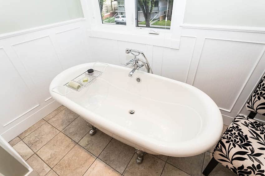 Bathroom with claw foot tub beige ceramic floor tile and light green walls white wainscoting