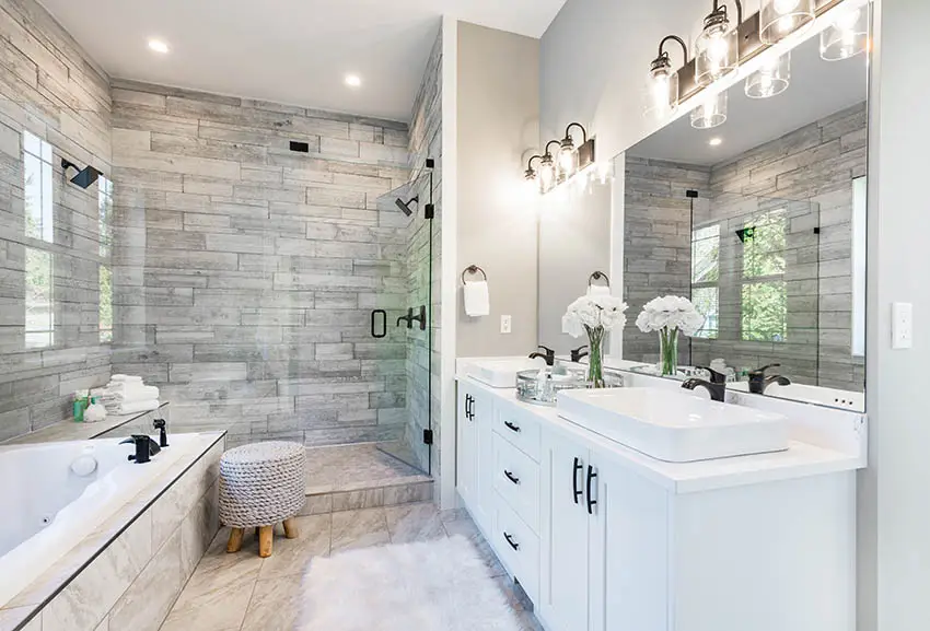 Bathroom with ceramic shower backsplash, vanity lights, bath tub and stool