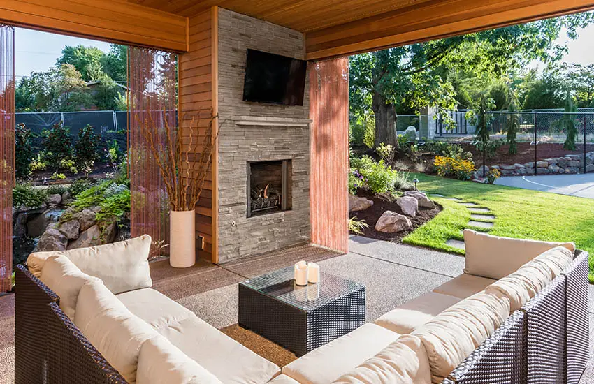 Covered patio with outdoor wind blocking shades wicker furniture stacked stone fireplace