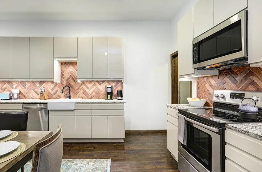 Kitchen with light gray lacquer cabinets herringbone pattern brick backsplash wood flooring