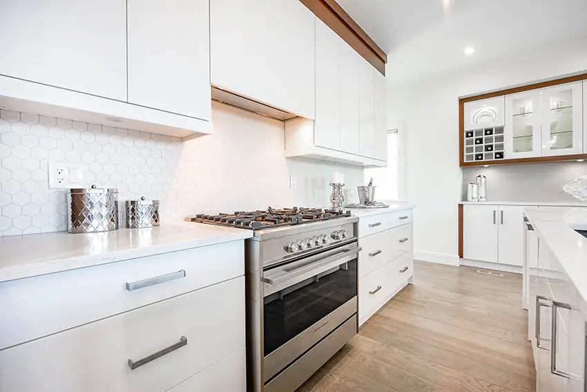 Kitchen with white lacquer cabinets white quartz hexagon shaped tile backsplash wood flooring