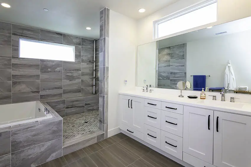 Built-in bathtub with slate walls, white vanity and rectangular windows