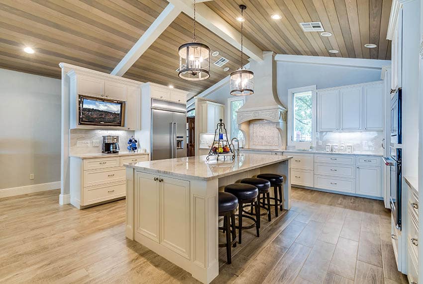 Large u shaped kitchen with light color countertops cream cabinets wood plank arched ceiling