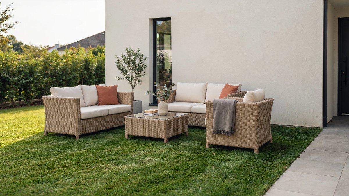 Woven wicker sectional and olive tree arranged on turf beside stucco wall