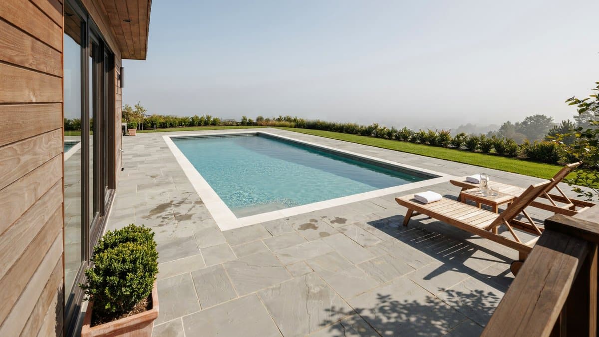Stone pool deck with turf border, teak loungers and distant valley haze