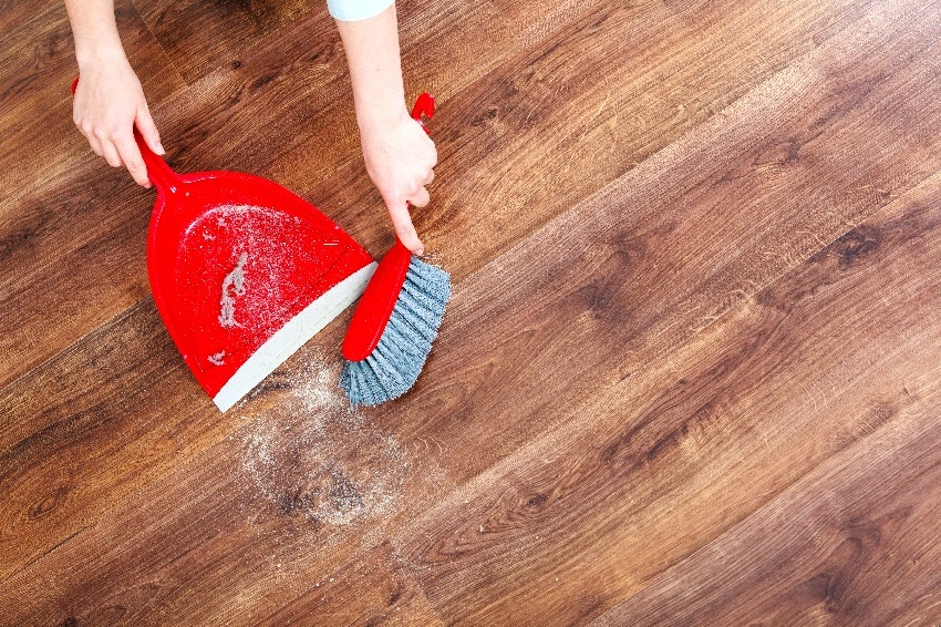 cleaning wood floor with whisk red broom and dustpan to keep furniture from sliding on wood floors