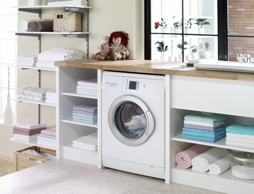 Electric dryer with wood countertop, white cabinets surrounded by clean clothing 