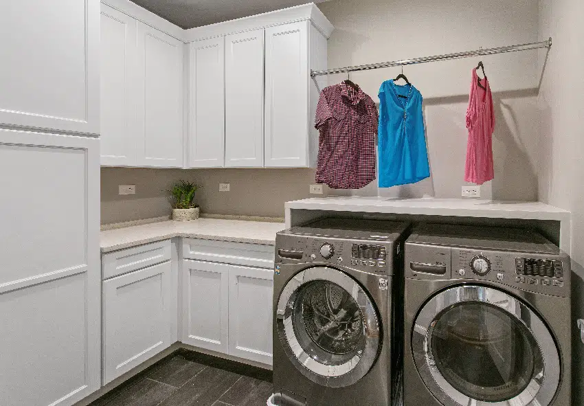 laundry room with white storage cabinets and hanged clothes on top of washer dryer