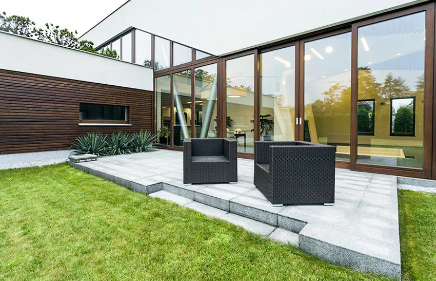 Modern concrete patio with glass folding door window wall rattan furniture and grass area