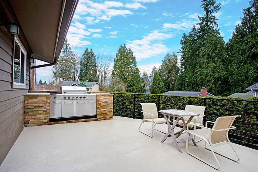 Deck with outdoor grill, white chairs and tables with house wood siding