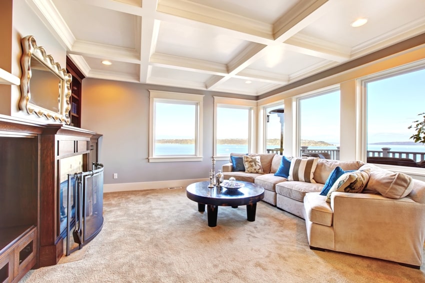 Room features coffered ceiling soft brown carpet floor comfortable sofa fireplace and coffee table