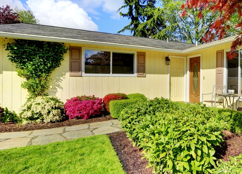 Yellow rambler style house with vertical siding with well kept flowerbed 