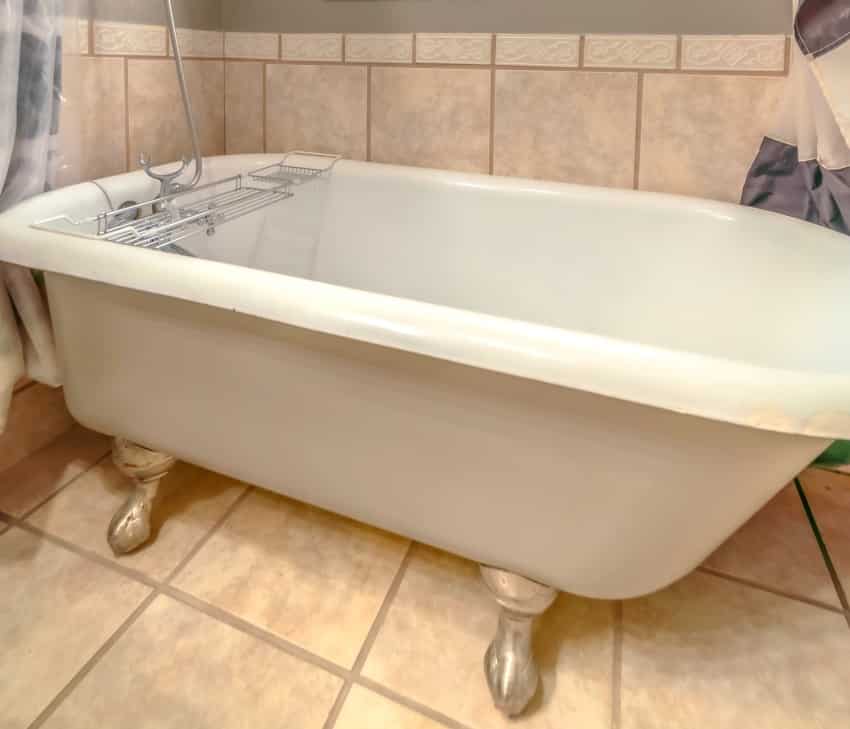 bathtub with some peeling marks on the corner and shower inside a bathroom with tiles on wall and floor