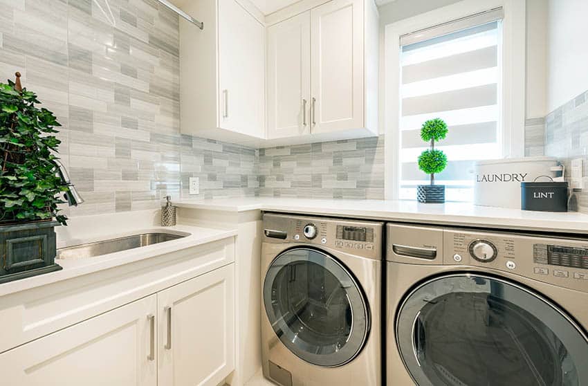 Beautiful laundry design with natural stone quartz countertops white cabinets tile backsplash stainless steel washer next to dryer