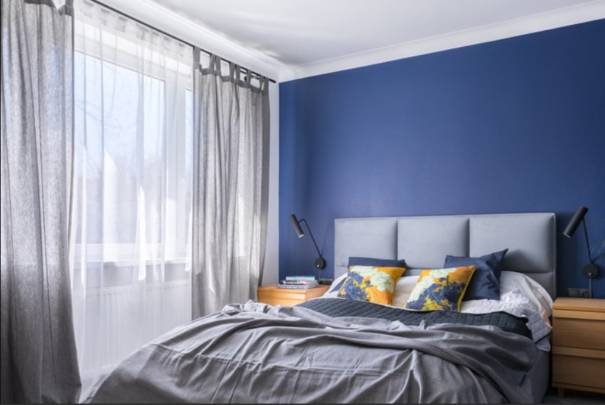 Bedroom with dark blue walls and gray and white curtains