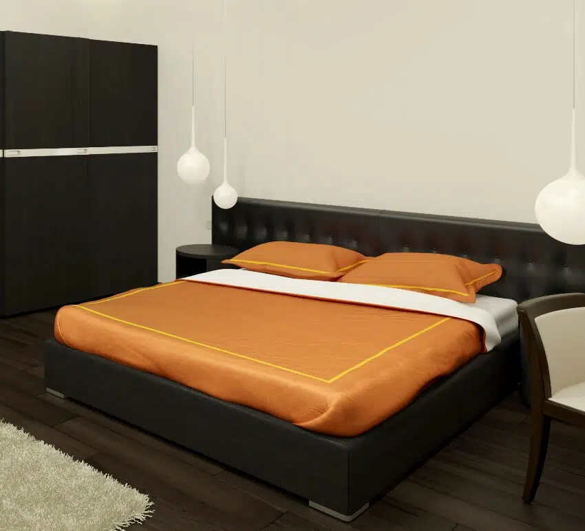Bedroom with dark wood floors bed frame and cabinets and a bed with orange pillows and blanket