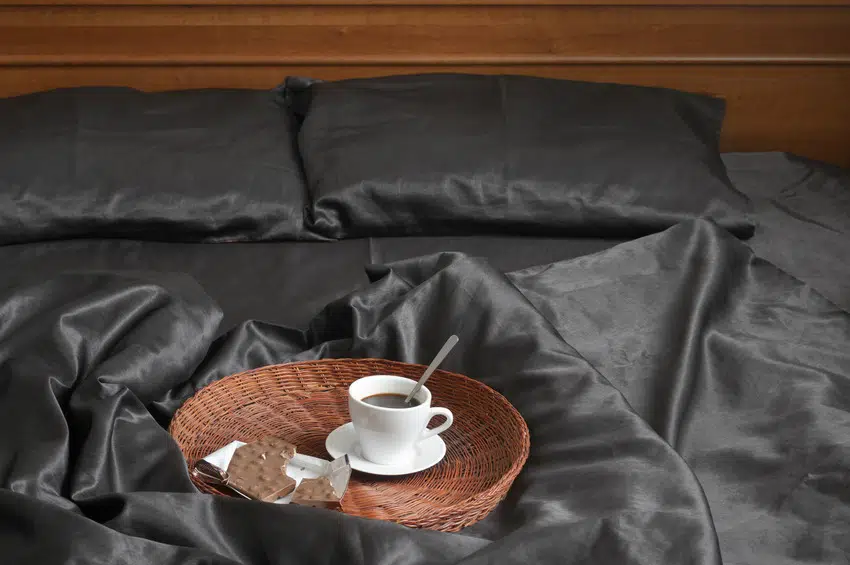 Breakfast tray on top of bed with dark silk bed sheet 