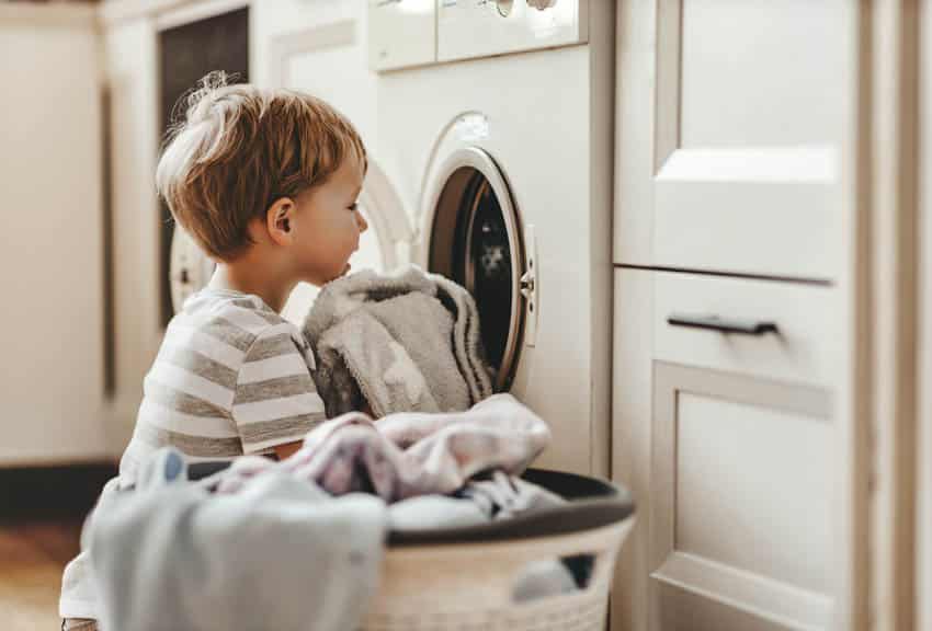 Child putting clothes in laundry machine with chute near him