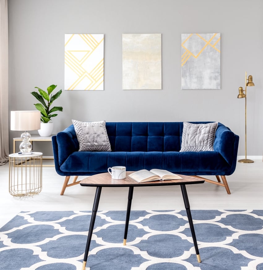 elegant interior with a blue sofa, patterned carpet and paintings on the gray background