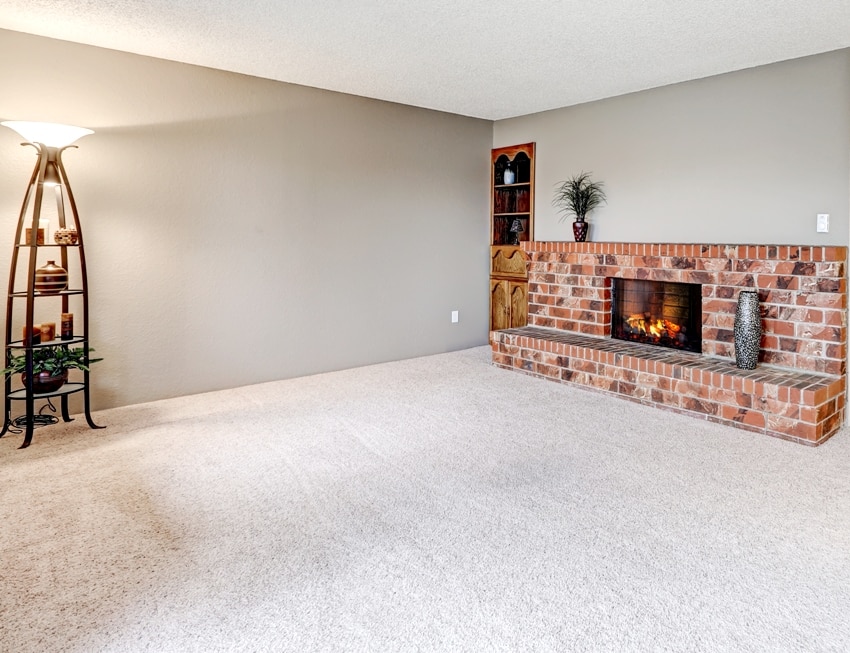 Empty living room features grey walls carpet floor and red brick fireplace