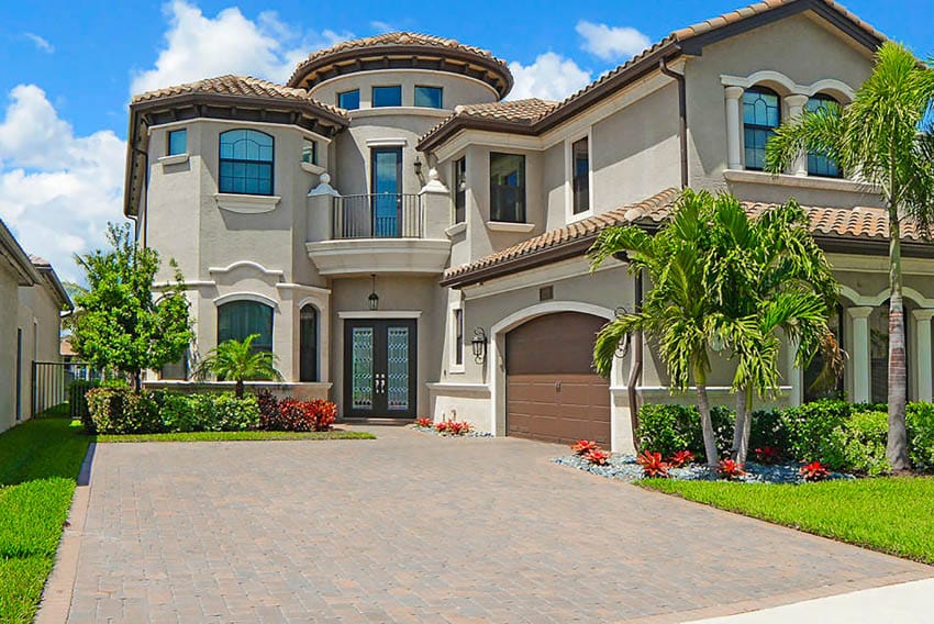 Glass and metal door in luxury mansion with concrete driveway and palm trees