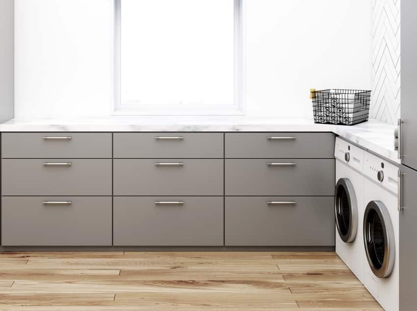 gray washroom corner with black wooden walls laminated flooring two washing machines and gray closets and countertops