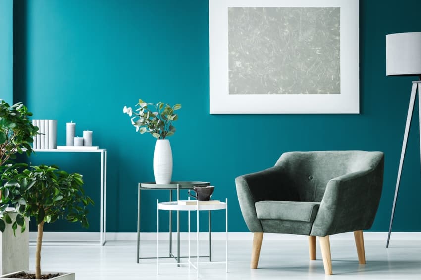 green armchair against teal painted wall with silver wall frame in living room interior with plants and floor lamp