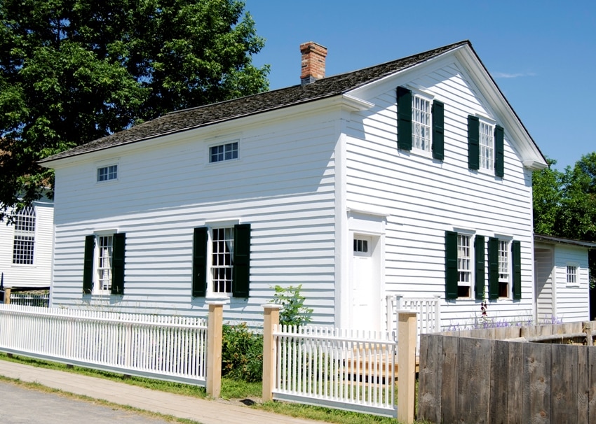 Home with white exterior shiplap, landscaped front yard with white wooden fence 