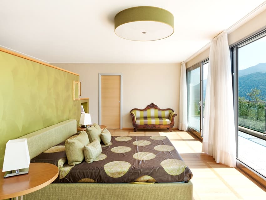 interior of a modern apartment bedroom with beige and yellow green theme glass doors white curtains and an ovelooking mountain view