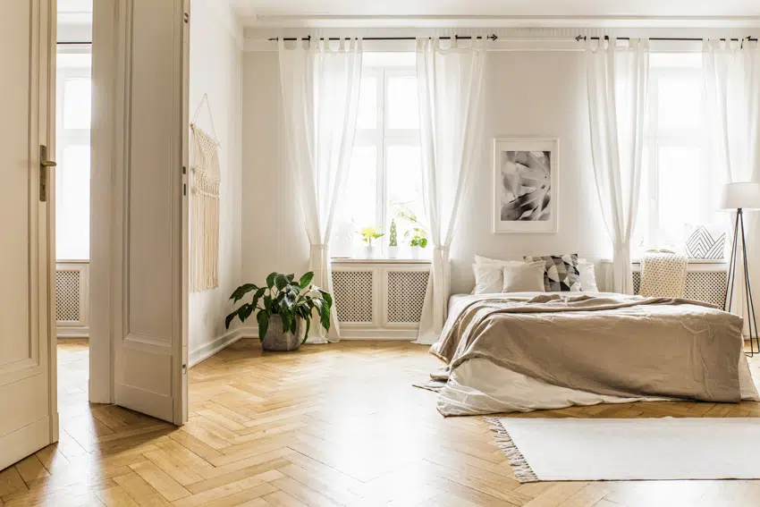 Master bedroom with white curtains wood flooring and indoor plant