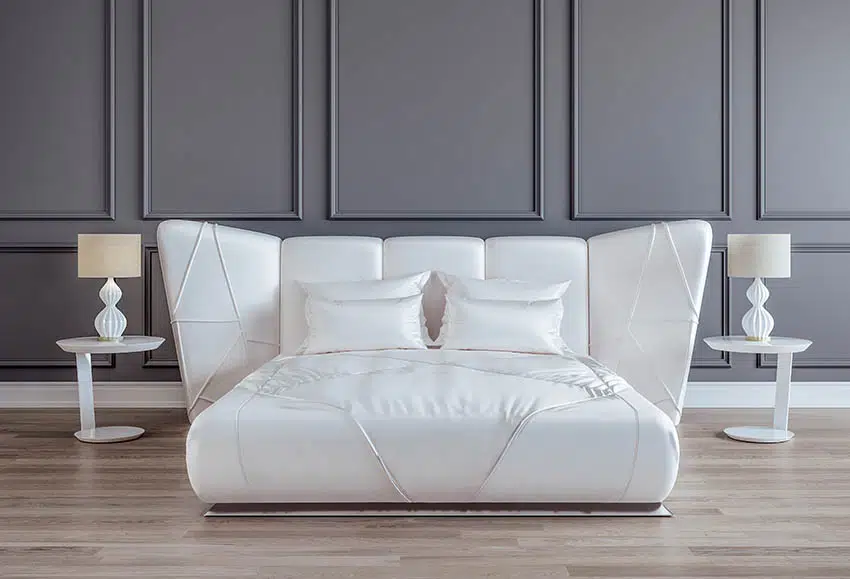 Modern bed with white satin sheets, pillows, headboard, lamps, and nightstands
