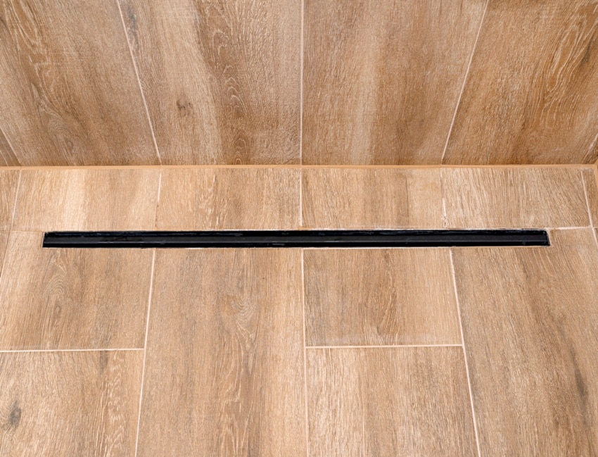 modern black linear drain in a bathroom lined with ceramic tiles imitating wood