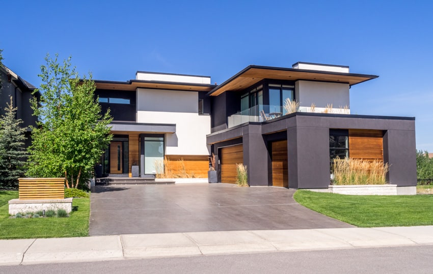 Modern house with spacious stained concrete finish driveway, windows, flat roof, and wood siding