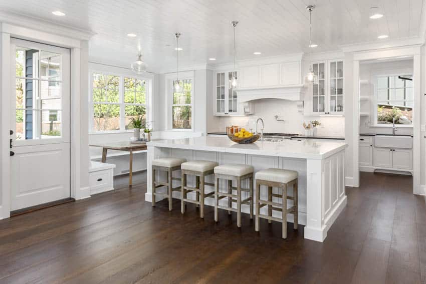 Modern kitchen with center island white stools dining booth area near window door and ceiling lights