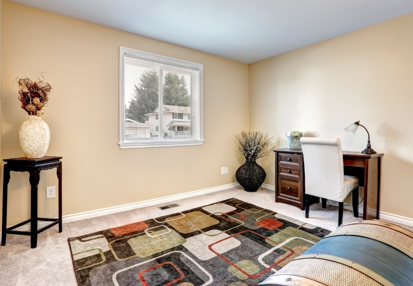 room with woodstock tan walls colorful rug small desk with white leather chair and wooden stand in the corner