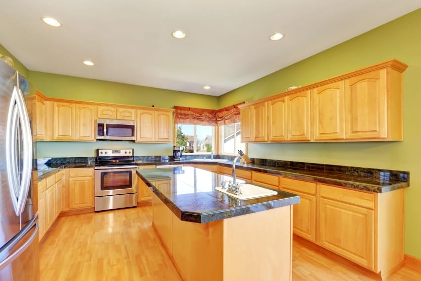 Spacious kitchen with green walls and hardwood floor has stainless steel appliances, kitchen island, maple storage, combination granite countertops, and honey oak cabinets