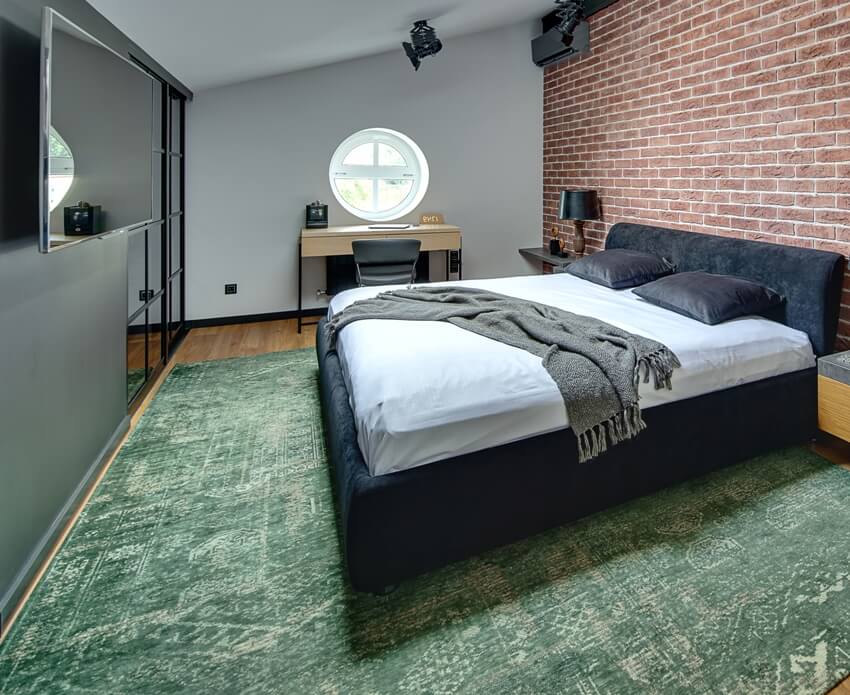 Stylish bedroom in modern style with brick wall and parquet with green carpet