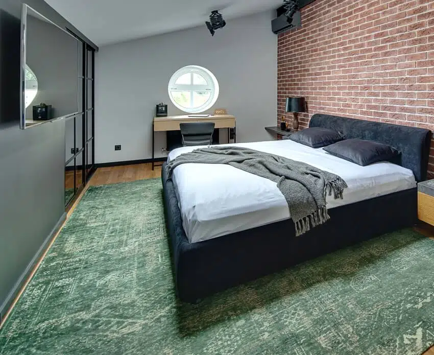 Stylish bedroom in modern style with brick wall and parquet with green carpet on the floor