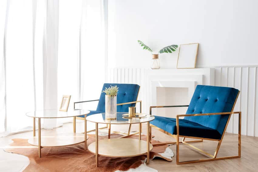 Two elegant comfortable blue armchairs and glass coffee table with gold accents