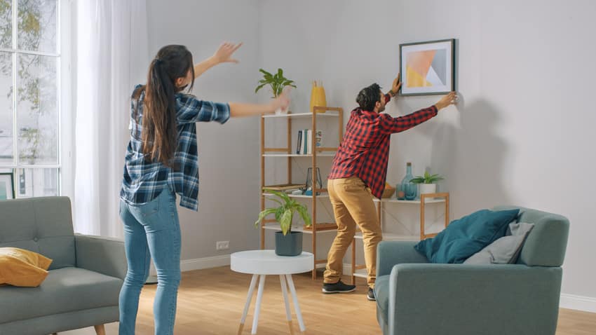 Woman instructing man how to hang frame on the wall