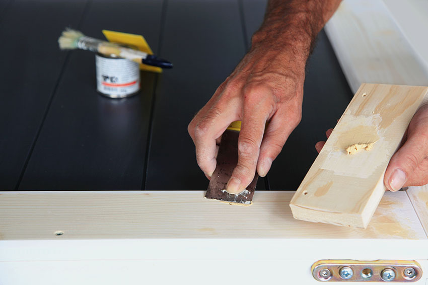 Applying wood putty to cabinet